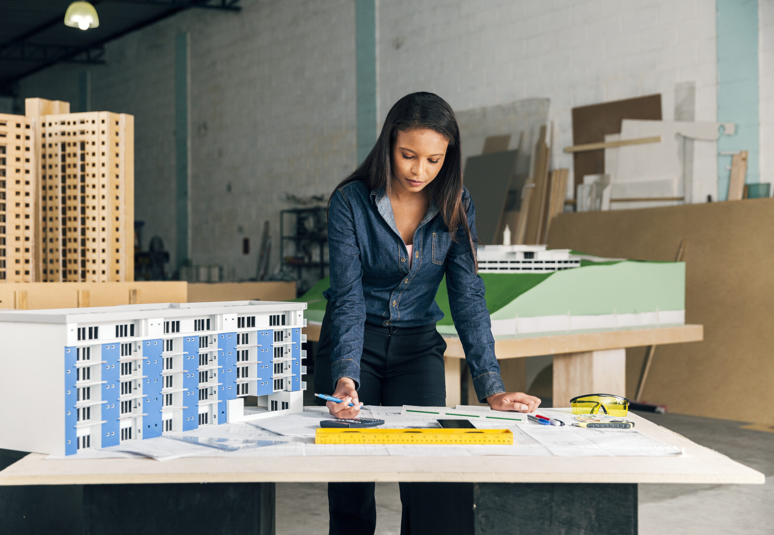 serious-african-american-lady-with-pen-standing-near-model-building-table buildbyher